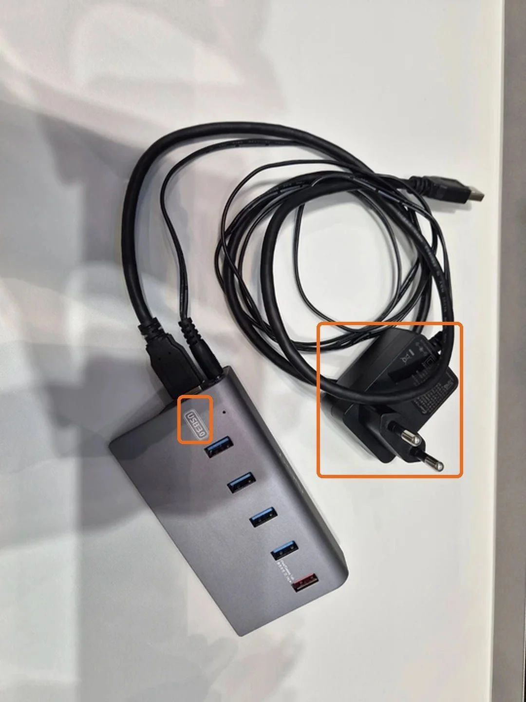 회색 USB 허브 몸체의 USB3.0 표기와 벽 콘센트에 꽂는 전원 어댑터를 주황 테두리로 표시한 사진